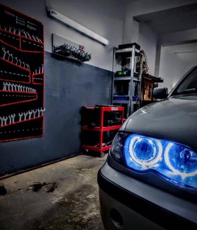 Werkplaats met een wand vol steeksleutels, een rood gereedschapswagentje en een BMW met blauwe lichtringen